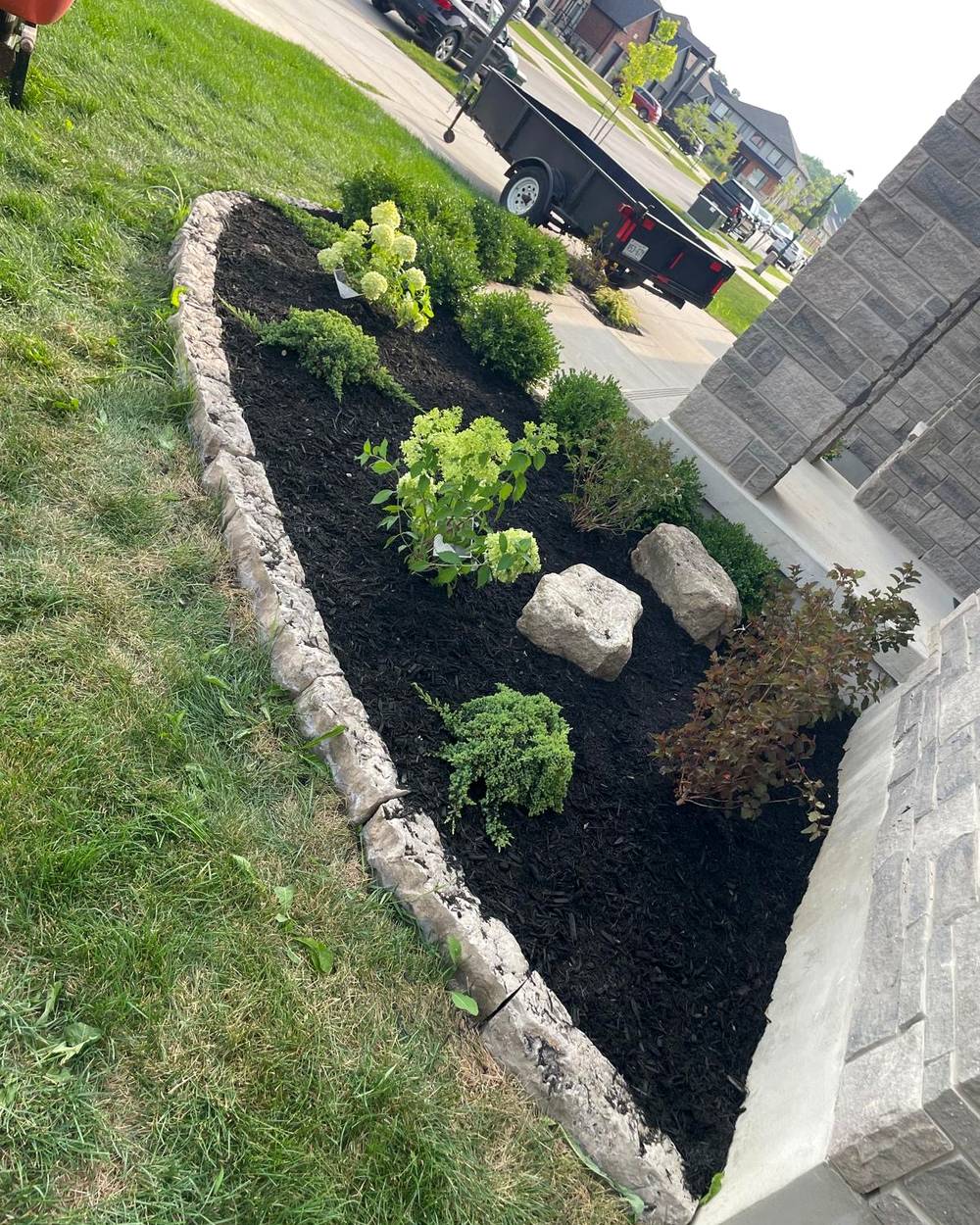 A finished armour stone garden bed with black mulch and plantings by TG Property Care in London