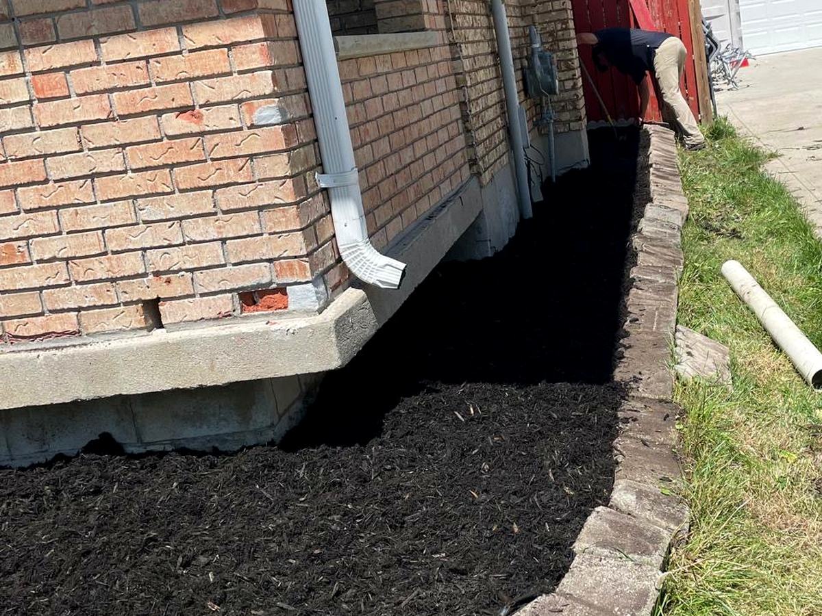 Black mulch bed with stone curb edging along a brick home